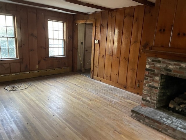 unfurnished living room featuring wooden walls, beam ceiling, a baseboard radiator, light hardwood / wood-style flooring, and a fireplace