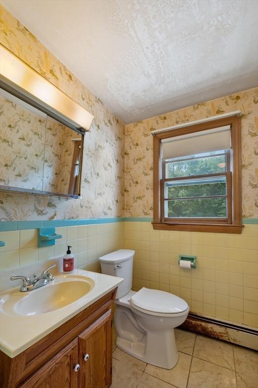 34 Buena Vista Ave, Salem, MA 01970 - bathroom featuring a baseboard heating unit, vanity, tile walls, tile patterned flooring, and a wainscoted wall