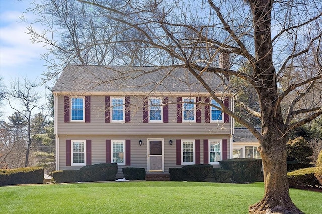 colonial house with a chimney, roof with shingles, and a front lawn