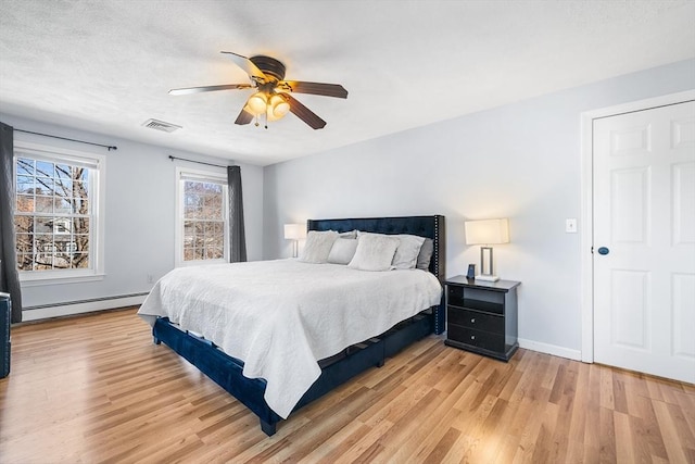 bedroom featuring baseboard heating, baseboards, light wood-type flooring, and visible vents