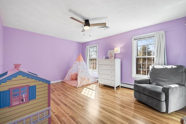 bedroom with visible vents, multiple windows, light wood-style flooring, and a baseboard heating unit