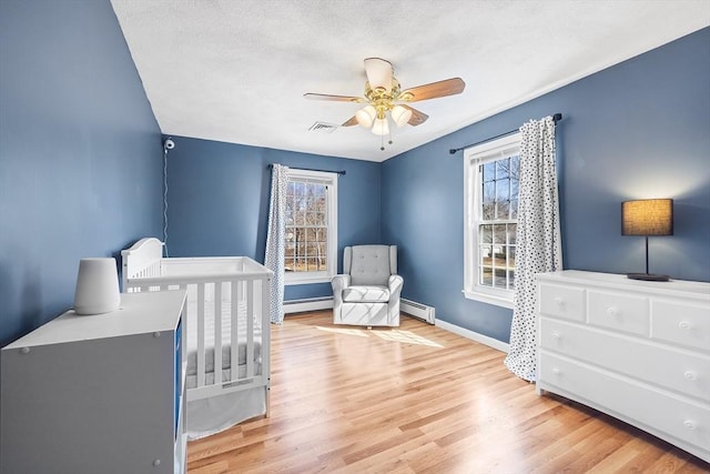 bedroom featuring visible vents, light wood-type flooring, and a baseboard heating unit