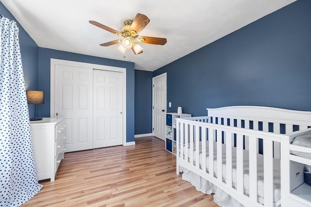 bedroom featuring a crib, a closet, light wood-style floors, baseboards, and ceiling fan