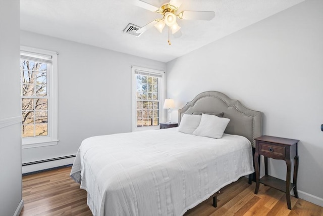 bedroom with a baseboard heating unit, baseboards, visible vents, and wood finished floors