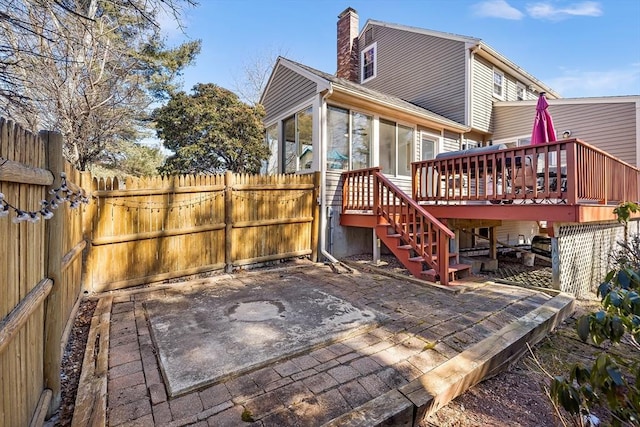 rear view of property with a wooden deck, a sunroom, a patio, and fence