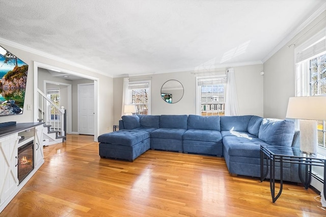 living area featuring stairway, a textured ceiling, ornamental molding, and light wood finished floors