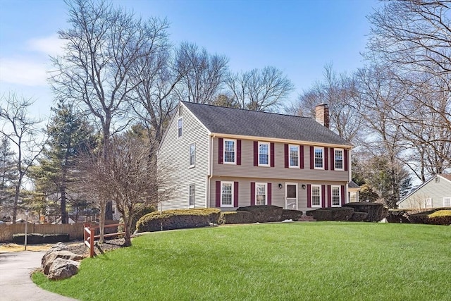 colonial home featuring a chimney, a front yard, and fence