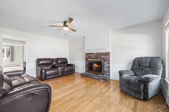 living area featuring light wood-style flooring, a fireplace, and a ceiling fan