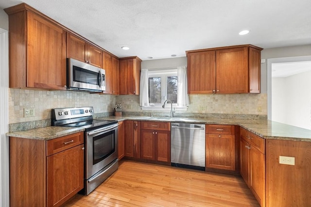 kitchen featuring brown cabinets, a peninsula, appliances with stainless steel finishes, light wood-style floors, and stone countertops