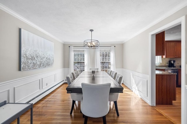 dining area featuring a wainscoted wall, a textured ceiling, wood finished floors, and a baseboard heating unit