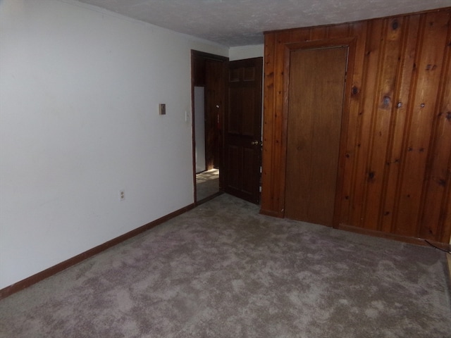 unfurnished bedroom with a closet, carpet, a textured ceiling, and wooden walls