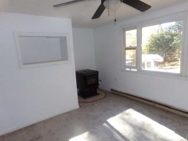 empty room with light carpet, a wood stove, a baseboard heating unit, and ceiling fan