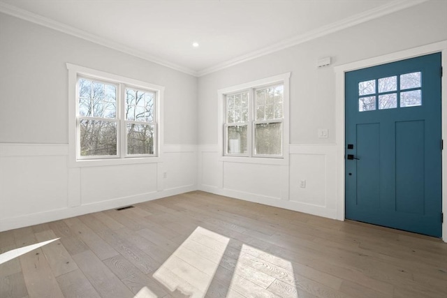 foyer entrance with wainscoting, ornamental molding, visible vents, and light wood-style flooring