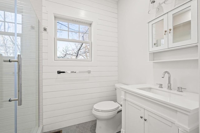 bathroom with toilet, vanity, a shower with door, and wood walls
