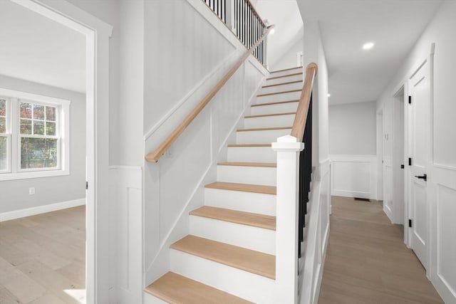 stairs with wainscoting, wood finished floors, recessed lighting, and a decorative wall