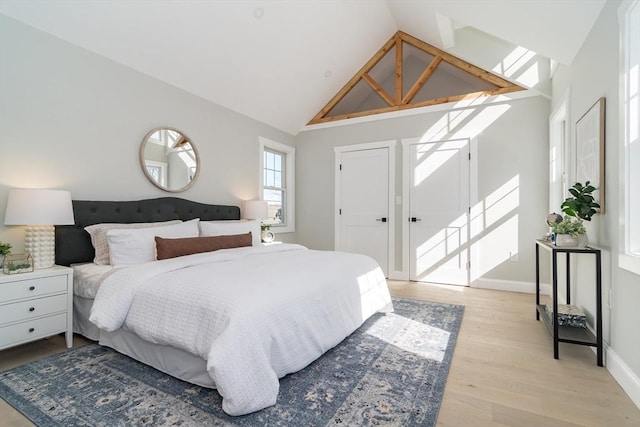 bedroom with light wood-style floors, baseboards, and high vaulted ceiling