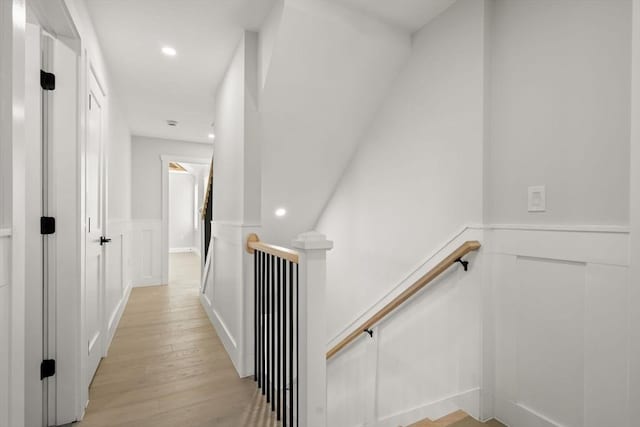 hallway featuring wainscoting, light wood-style flooring, an upstairs landing, and a decorative wall