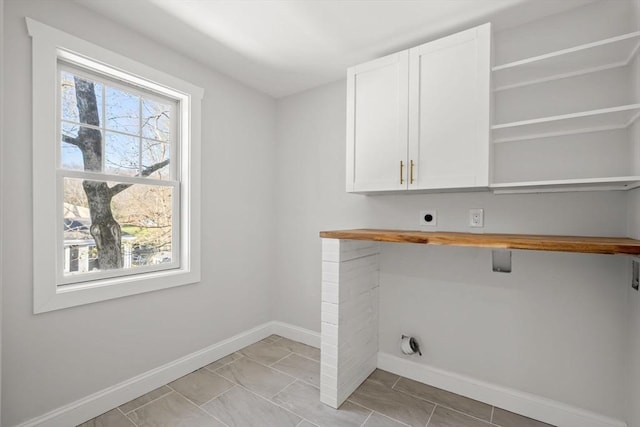 laundry room featuring electric dryer hookup, baseboards, and cabinet space