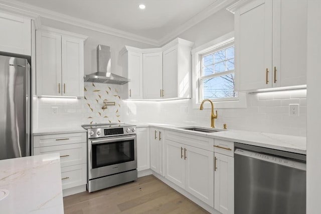 kitchen with stainless steel appliances, a sink, white cabinetry, wall chimney range hood, and light stone countertops