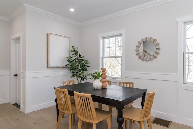 dining space with crown molding, visible vents, light wood-type flooring, and a decorative wall