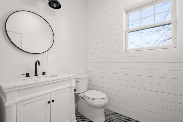 half bath with toilet, vanity, and wood walls