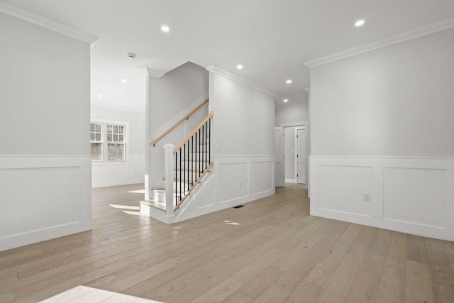 unfurnished living room featuring a decorative wall, ornamental molding, and stairs