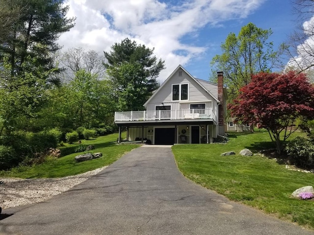 view of front of property with an attached garage, a deck, a front yard, a chimney, and asphalt driveway