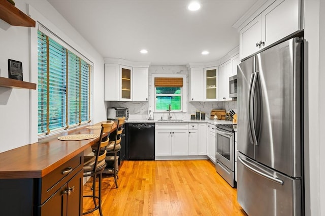 kitchen with stainless steel appliances, decorative backsplash, a sink, white cabinets, and glass insert cabinets