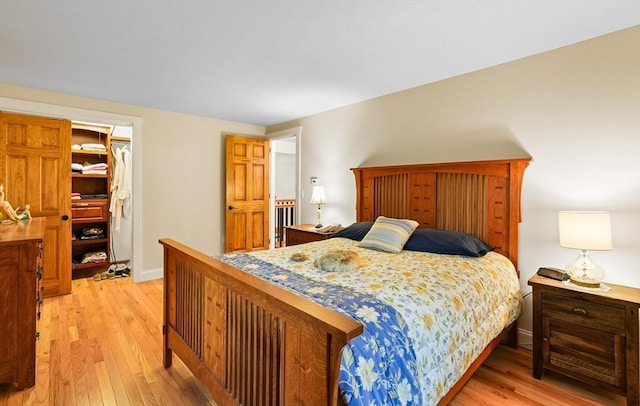 bedroom with light wood finished floors, a spacious closet, a closet, and baseboards
