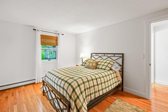 bedroom with wood finished floors, a baseboard heating unit, and baseboards