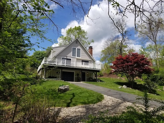 view of front of house featuring an attached garage, a chimney, a front yard, driveway, and a deck