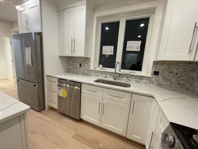 kitchen with light stone countertops, a sink, white cabinets, light wood-style floors, and appliances with stainless steel finishes