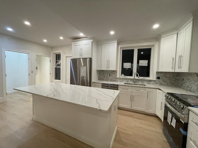 kitchen with a sink, light wood-type flooring, a kitchen island, and appliances with stainless steel finishes