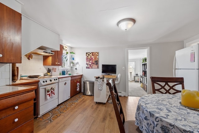 kitchen with light wood-type flooring, backsplash, white appliances, sink, and white cabinetry