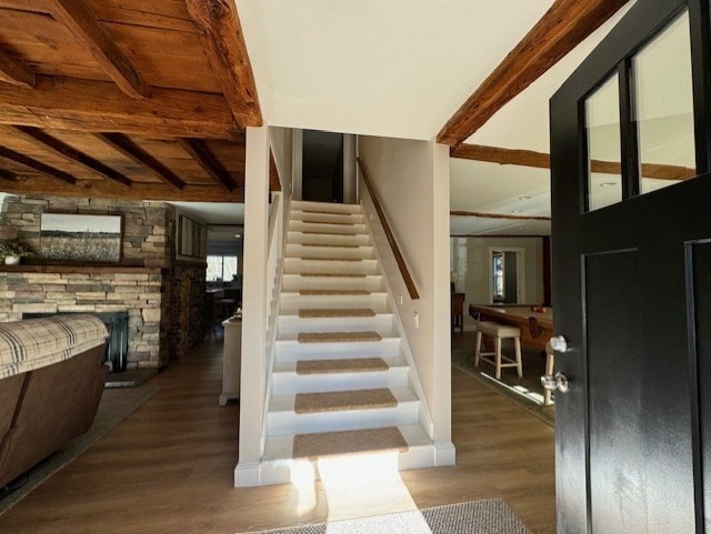 stairway with hardwood / wood-style floors, a stone fireplace, and beamed ceiling