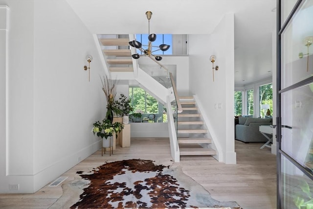 foyer entrance featuring an inviting chandelier, stairway, wood finished floors, and visible vents