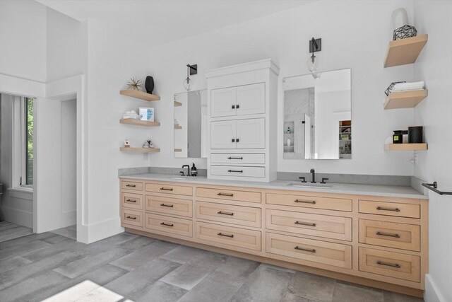 bathroom featuring a sink, double vanity, walk in shower, and baseboards