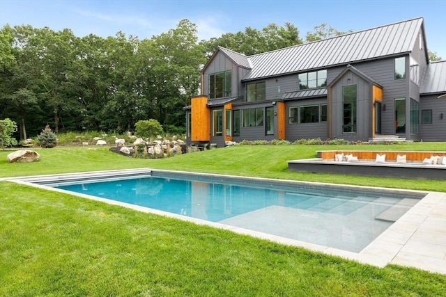 rear view of property featuring metal roof, a lawn, a standing seam roof, and an outdoor pool