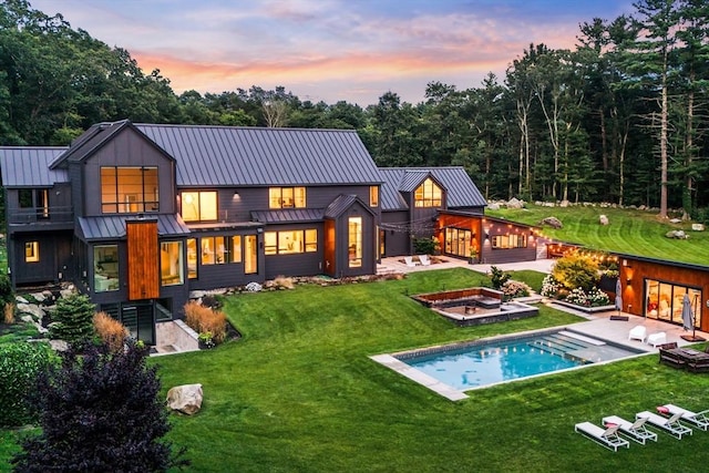 rear view of house featuring metal roof, an outdoor pool, a standing seam roof, and a lawn