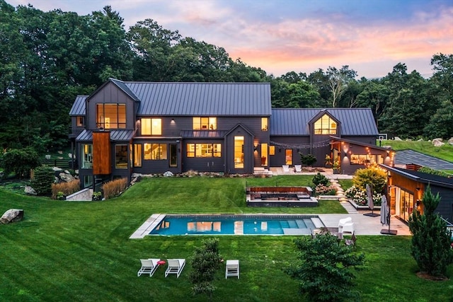 back of property at dusk with a patio area, an outdoor pool, a yard, metal roof, and a standing seam roof
