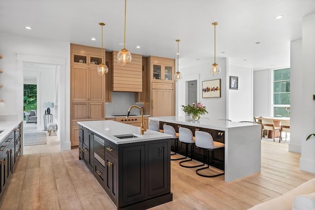 kitchen with an island with sink, light wood finished floors, light countertops, and glass insert cabinets