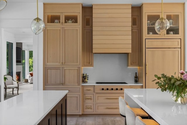 kitchen with light countertops, wall chimney exhaust hood, glass insert cabinets, and decorative light fixtures
