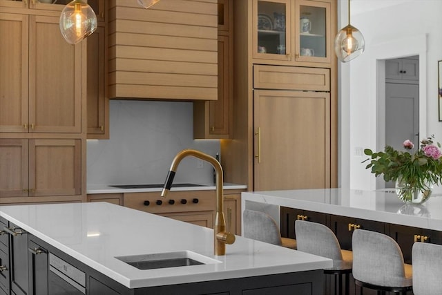 kitchen with glass insert cabinets, a sink, a kitchen island with sink, decorative light fixtures, and light countertops