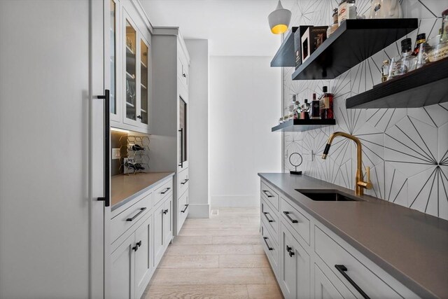 bar featuring bar area, baseboards, light wood finished floors, a sink, and decorative backsplash
