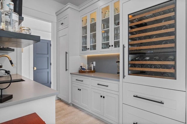 bar featuring a sink, beverage cooler, and light wood-style floors