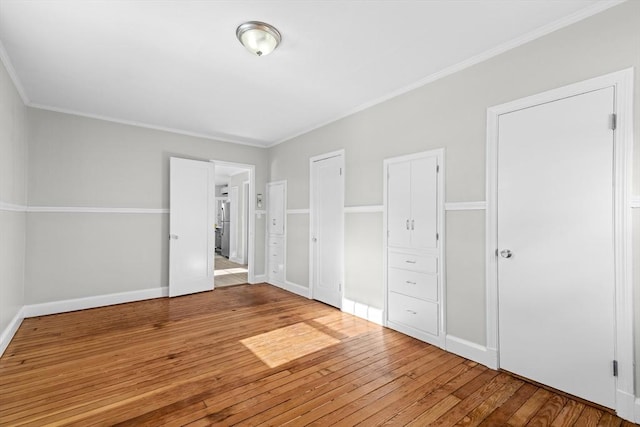 unfurnished bedroom with crown molding, hardwood / wood-style flooring, and two closets