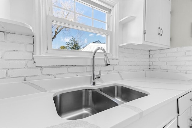 interior details with white cabinetry, sink, and light stone counters