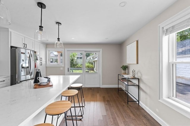 kitchen featuring stainless steel fridge, a kitchen breakfast bar, a wealth of natural light, pendant lighting, and white cabinets