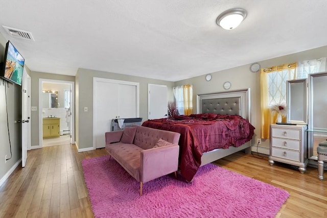 bedroom with ensuite bath, light hardwood / wood-style floors, and baseboard heating