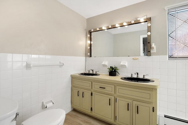 bathroom featuring toilet, tile walls, baseboard heating, vanity, and hardwood / wood-style flooring